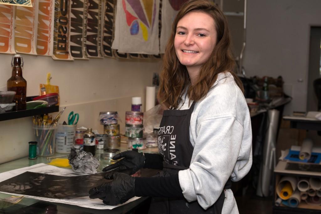 A student wears an apron and gloves while screenprinting at an internship