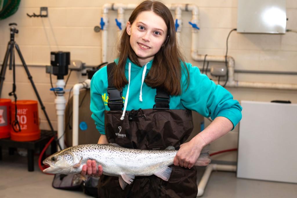 A student wearing work overalls holds up a fish in the Marine Science Center