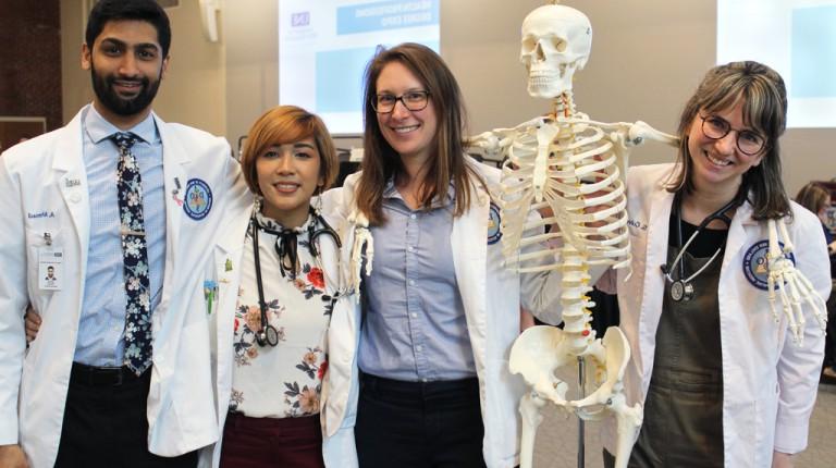 Four U N E osteopathic medicine students pose with an educational skeleton