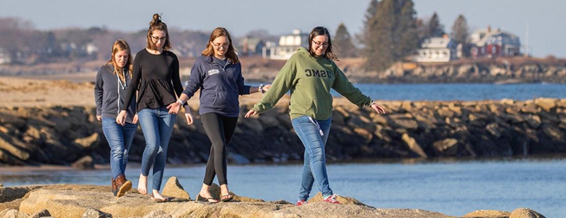 Four students walking on the rocks along the ocean