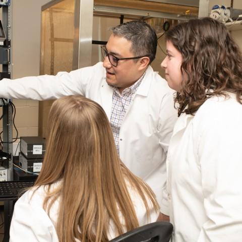 Three UNE researchers examine a microscope